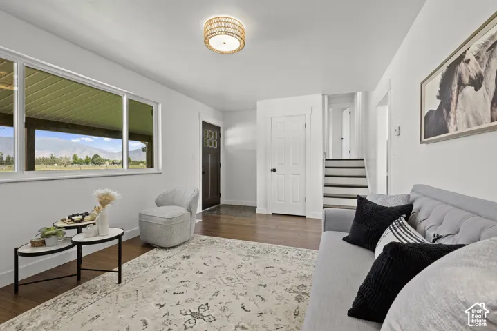 Hardwood flooring, white painted walls, large window with outdoor scenery, recessed stairway, and a decorative ceiling light fixture