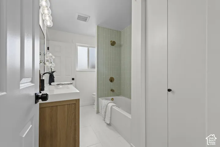 Spa-inspired bathroom featuring a wood-finish vanity with integrated sink and matte black hardware, white subway tile walls, and a soaking tub with green vertical tile surround