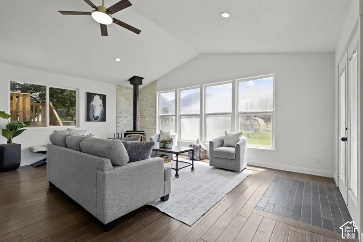 Vaulted ceiling with ceiling fan, expansive windows, wood-finish flooring, built-in wood-burning stove, and a stone-clad wall accent