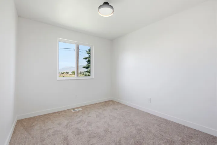 Carpeted room featuring a single window, white walls, and a ceiling-mounted light fixture