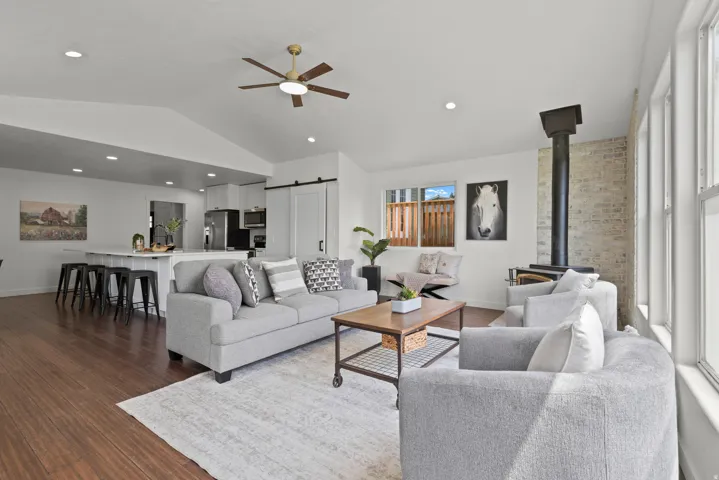Vaulted ceilings, wood-finish flooring, white walls, exposed brick accent, and a built-in wood stove