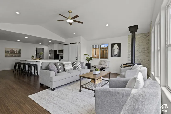 Vaulted ceilings, wood-finish flooring, white walls, exposed brick accent, and a built-in wood stove