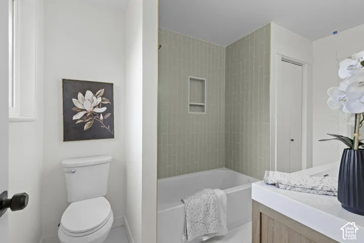 Bathtub with subway tile surround, integrated shower niche, and a light wood-finish vanity with a white countertop
