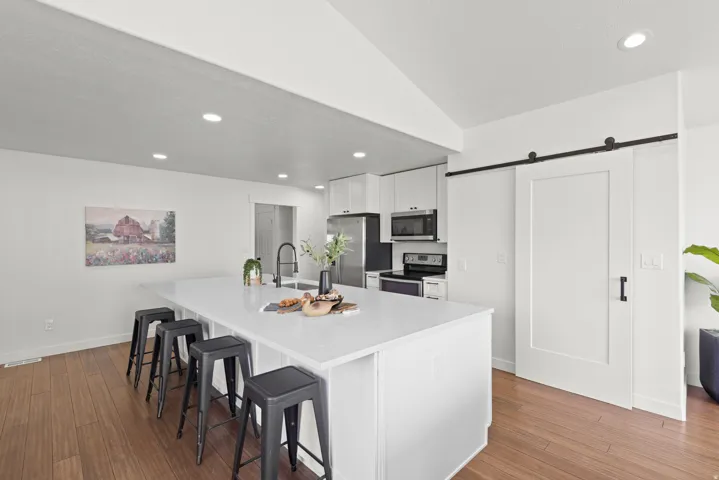 Spacious kitchen featuring a large island with an integrated sink, stainless steel appliances, white cabinetry, and wood-finish flooring