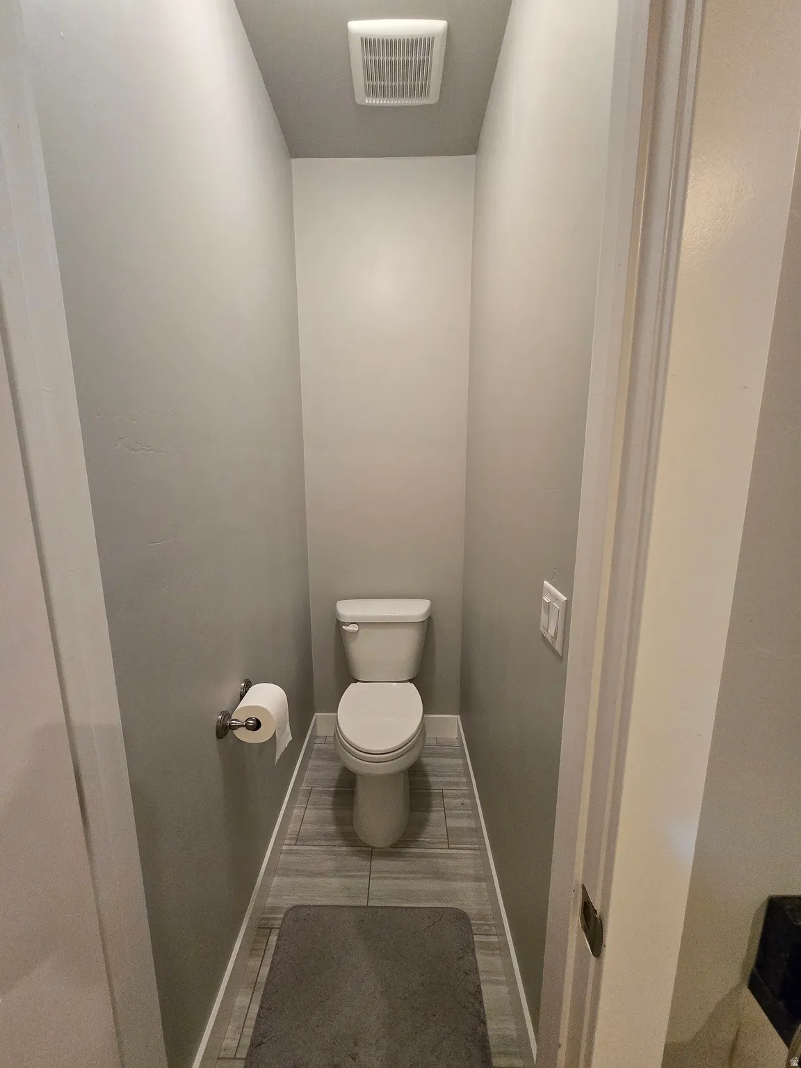 Powder room featuring a white toilet, gray wall paint, and wood-look tile flooring