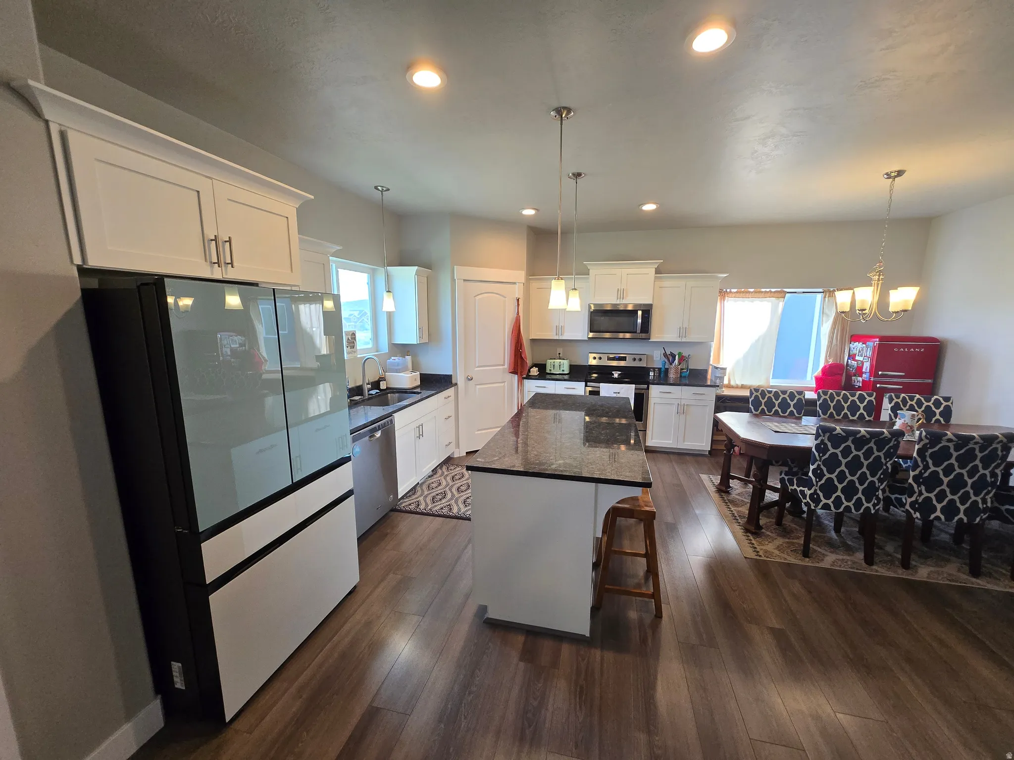 Open-concept kitchen and dining area featuring wood-finish flooring, white cabinetry with crown molding, a kitchen island with a dark countertop, and recessed lighting