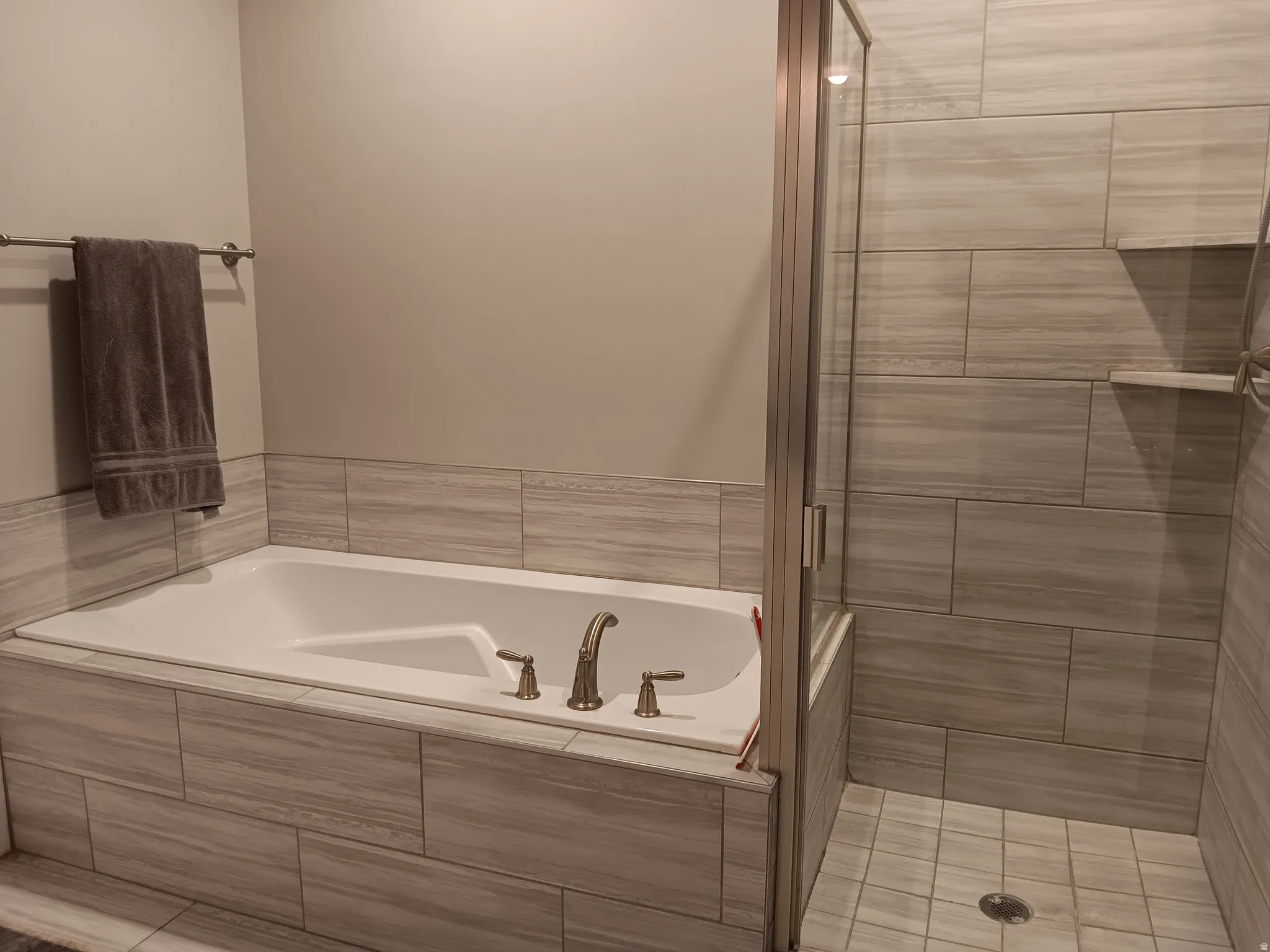 Soaking tub with brushed nickel fixtures, light-toned wood-finish tile surround, and an adjacent walk-in shower with clear glass enclosure