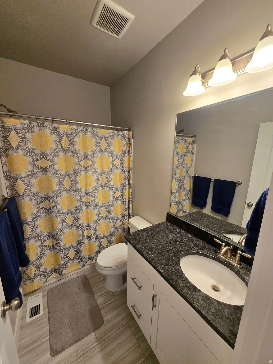 Bathroom featuring a single vanity with dark granite countertop, a white under-mount sink, and brushed nickel fixtures