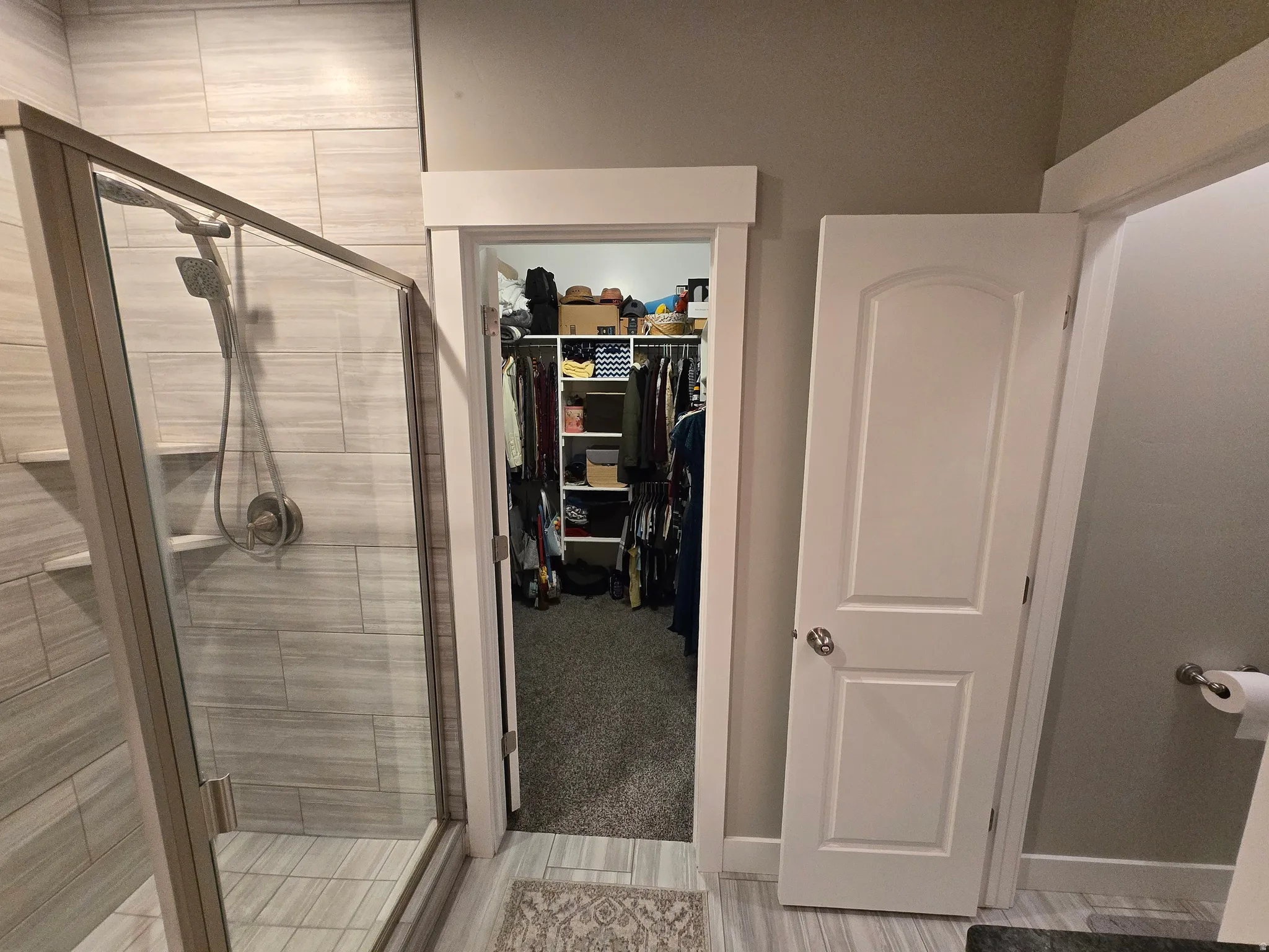 Glass-enclosed shower with light-toned tiled walls and flooring, featuring a built-in shower niche and brushed nickel fixtures