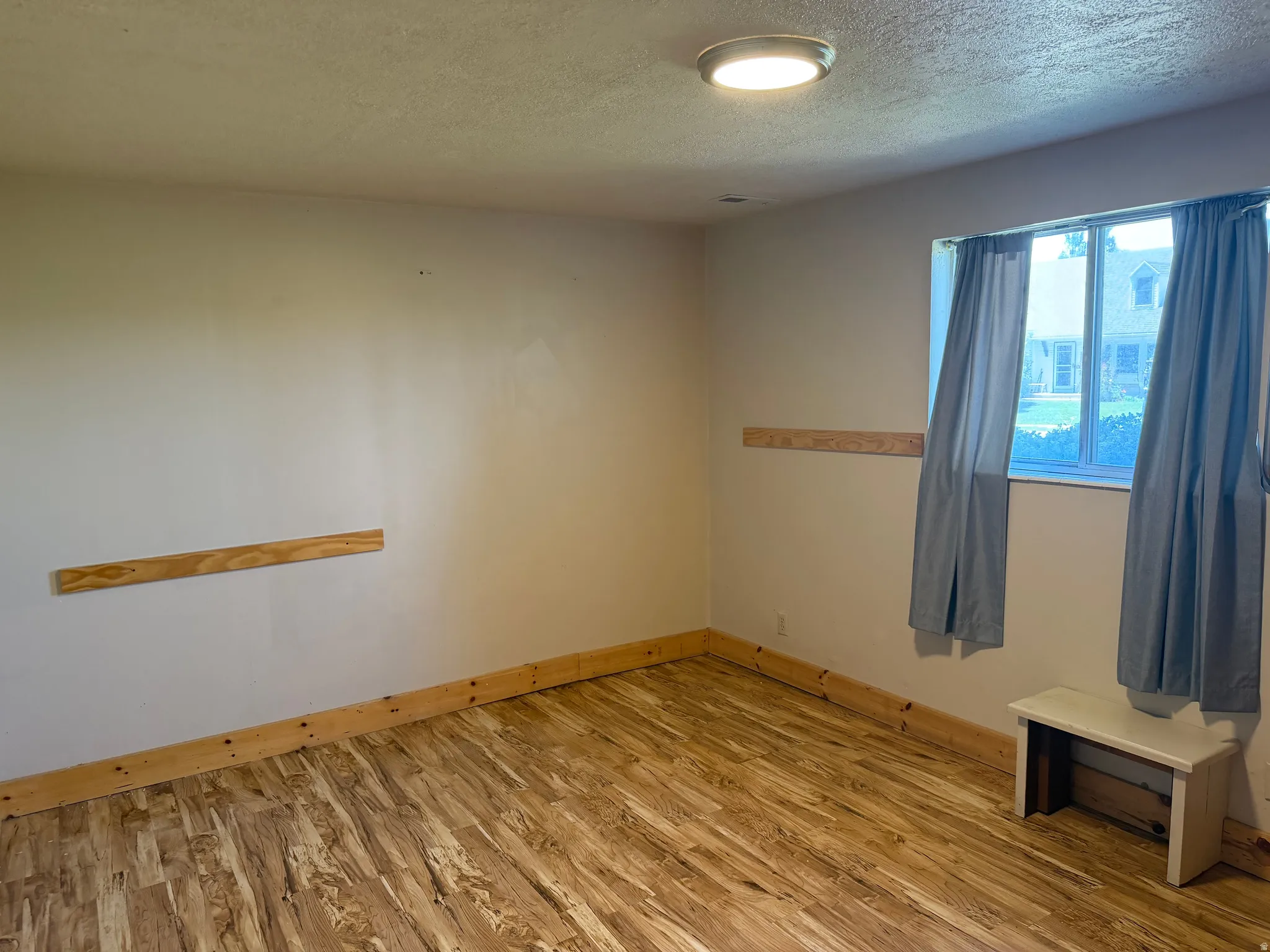 Room featuring wood-finish flooring, a window with window treatments, and light-toned walls