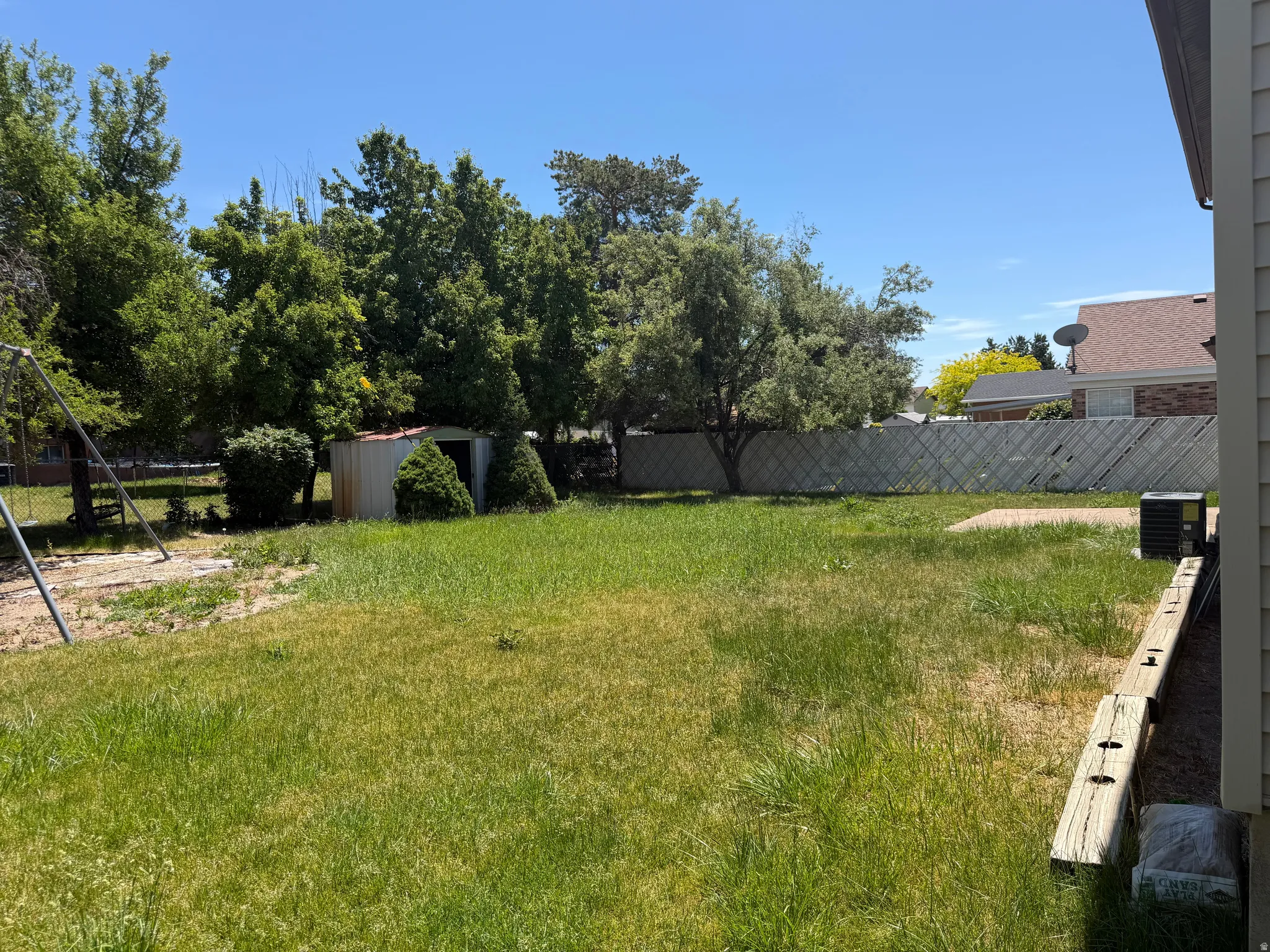 Expansive grassy yard featuring mature trees, a storage shed, a concrete patio, and a privacy fence