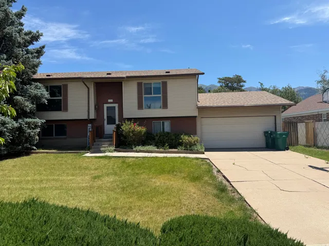 Split-level residence featuring a two-car garage, front lawn, and mature evergreen landscaping