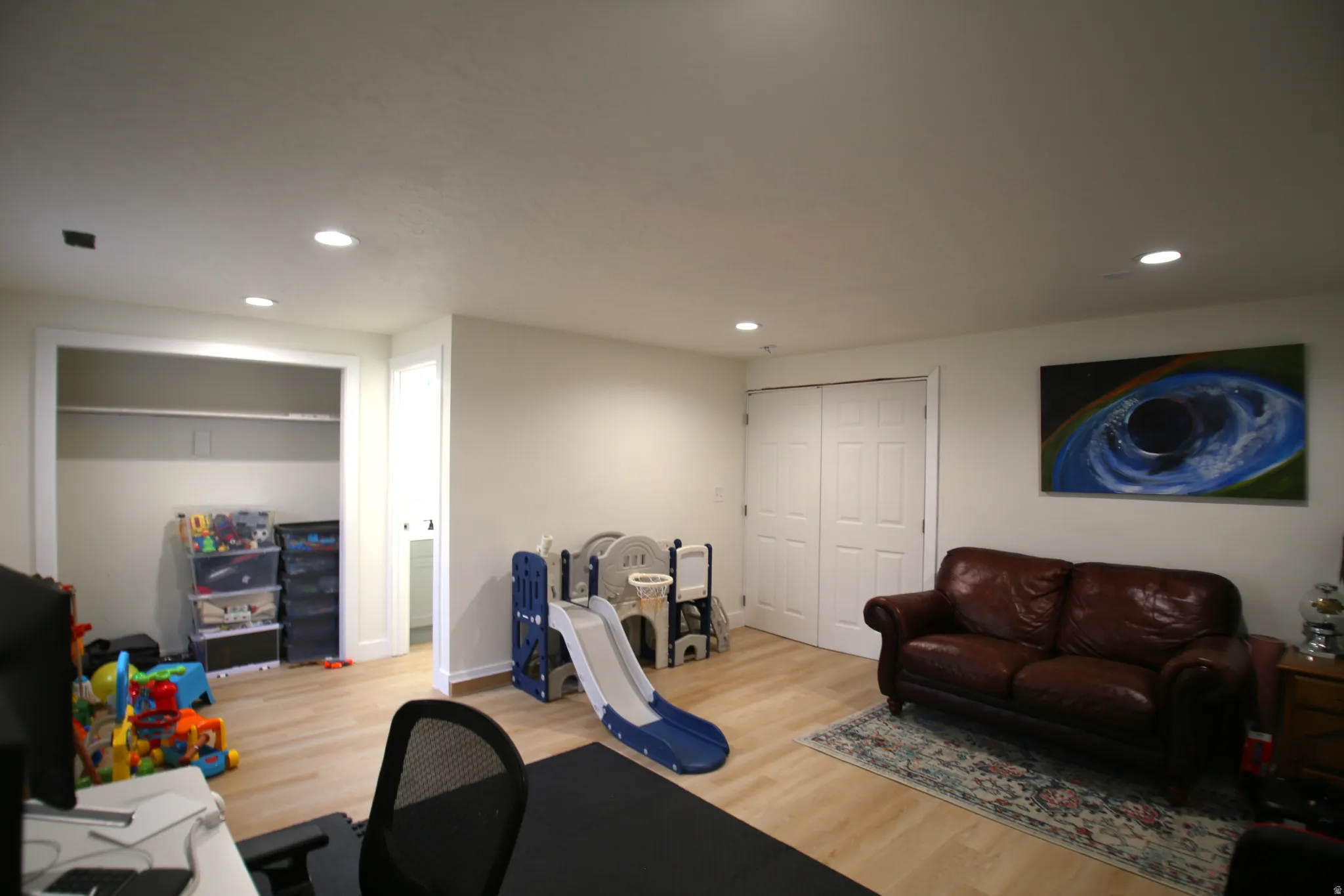 Spacious room featuring light wood-finish flooring, recessed lighting, and white walls