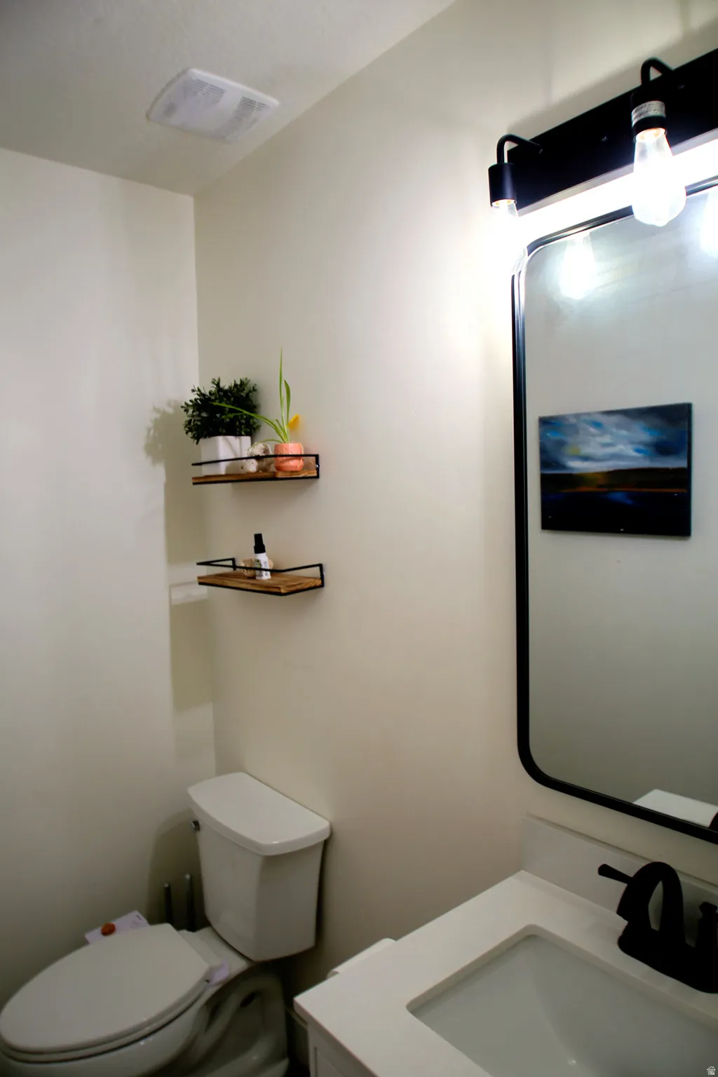 Bathroom featuring a white toilet, white vanity with integrated sink, matte black faucet, and a large black-framed mirror