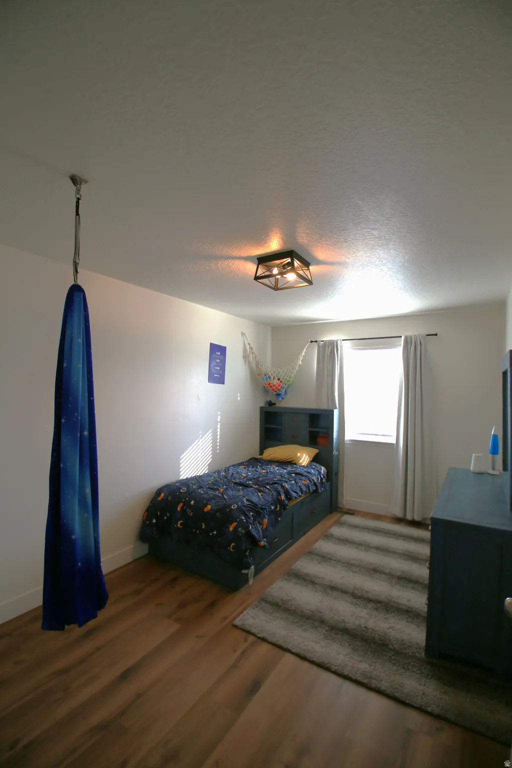 Room featuring wood-finish flooring, white walls, and a window with blinds and curtains