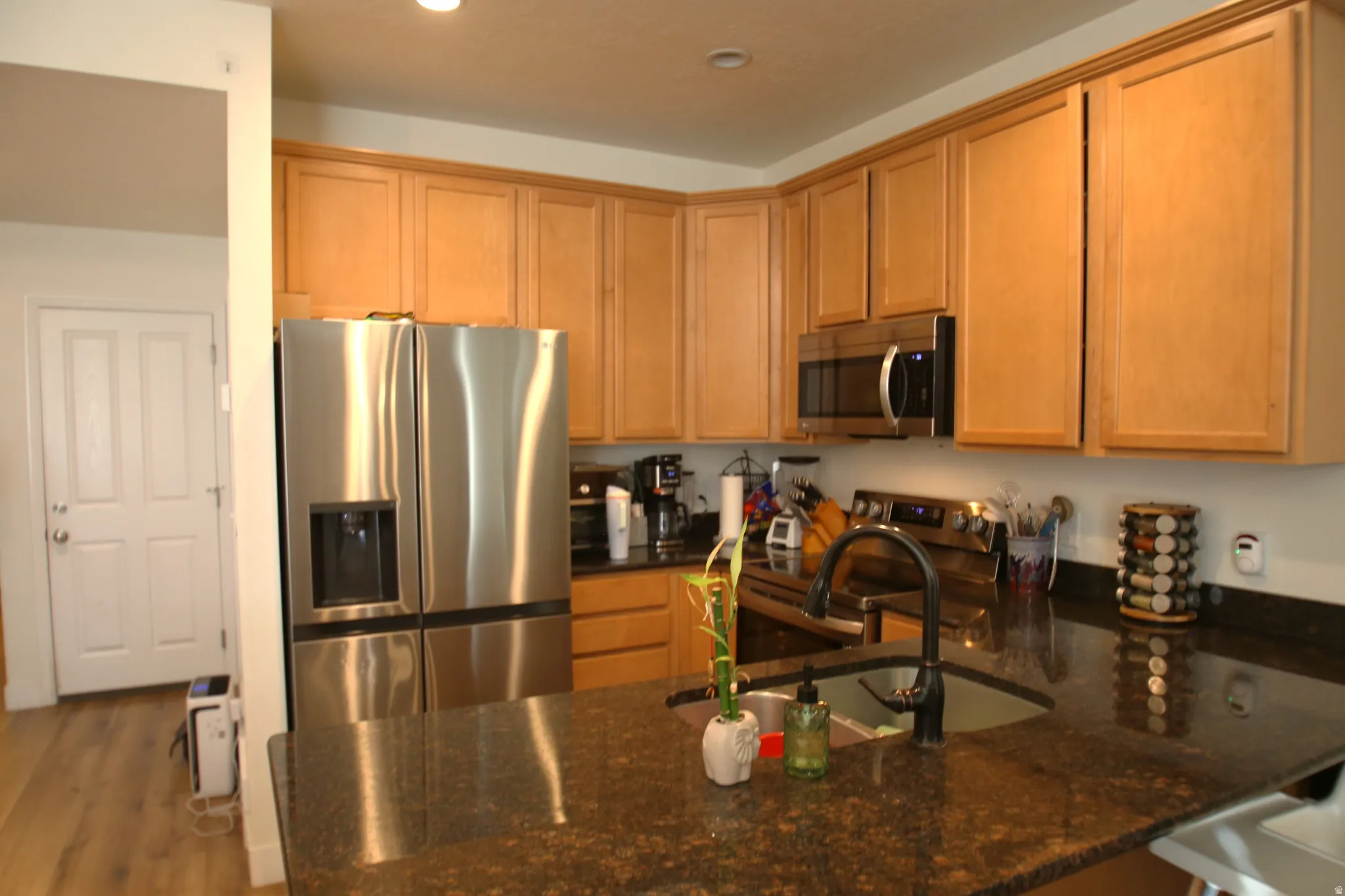 Kitchen featuring stainless steel appliances, wood cabinetry, dark granite countertops, and wood-finish flooring
