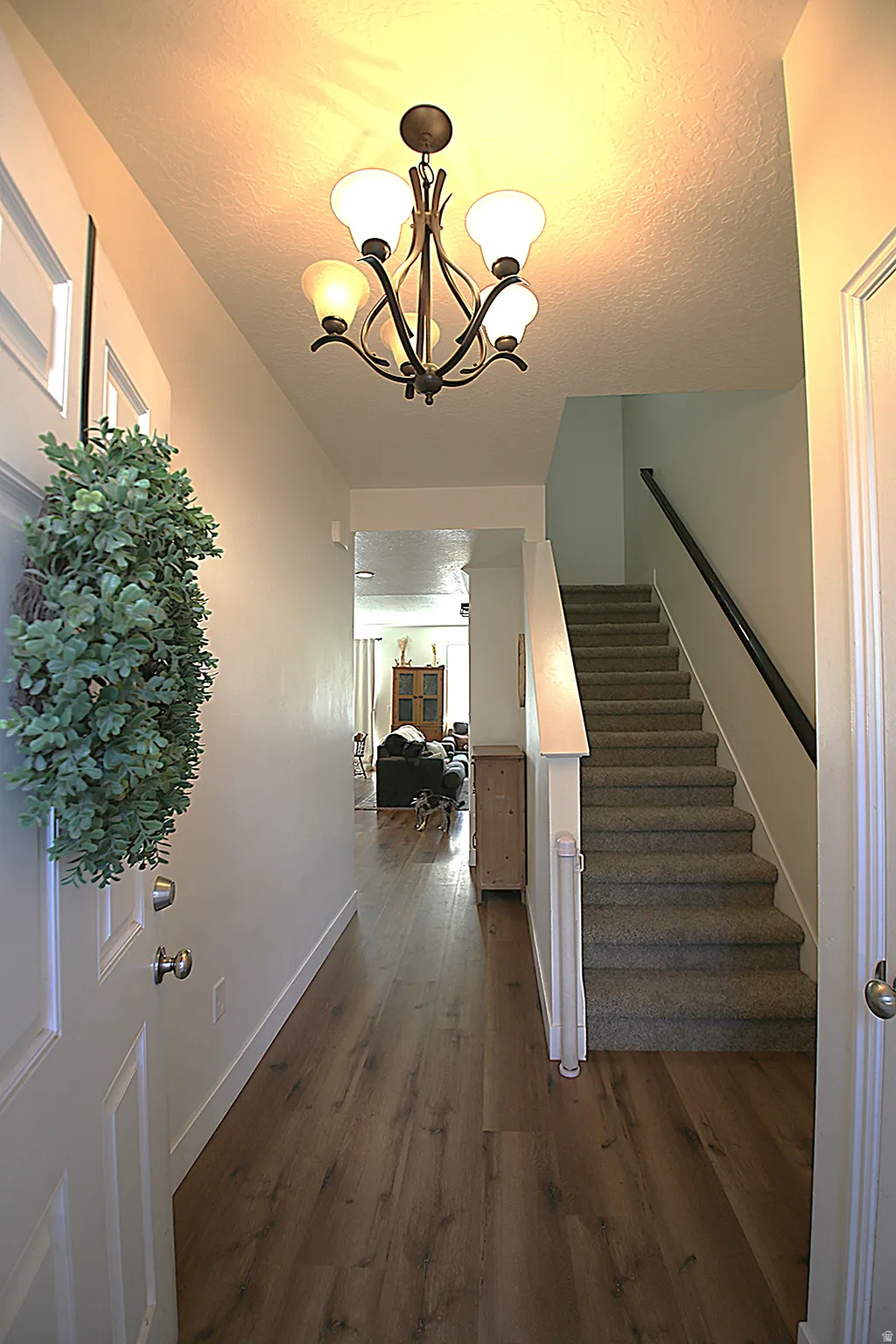Foyer entry featuring wood-finish flooring, a contemporary chandelier, and a carpeted staircase with a white baluster and dark handrail