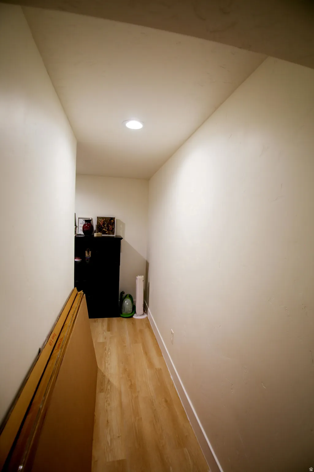 Recessed ceiling lighting illuminates a hallway featuring wood-finish flooring and white baseboards