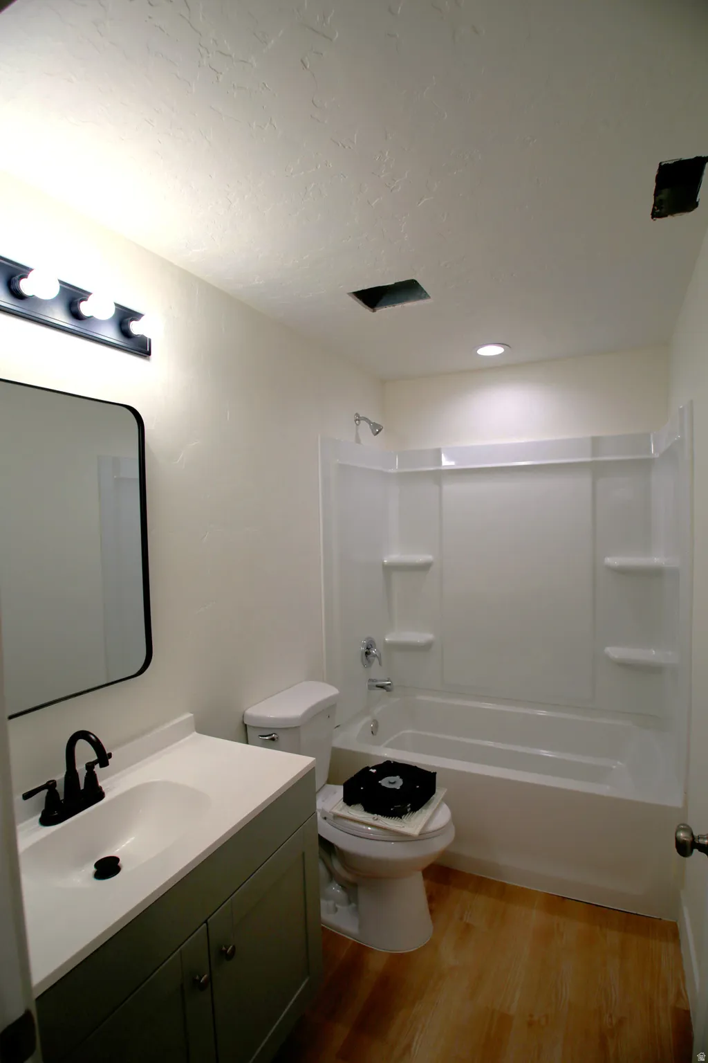 Bathroom featuring a modern vanity with integrated sink, a rectangular mirror, a shower-tub combination with white surround, and wood-finish flooring