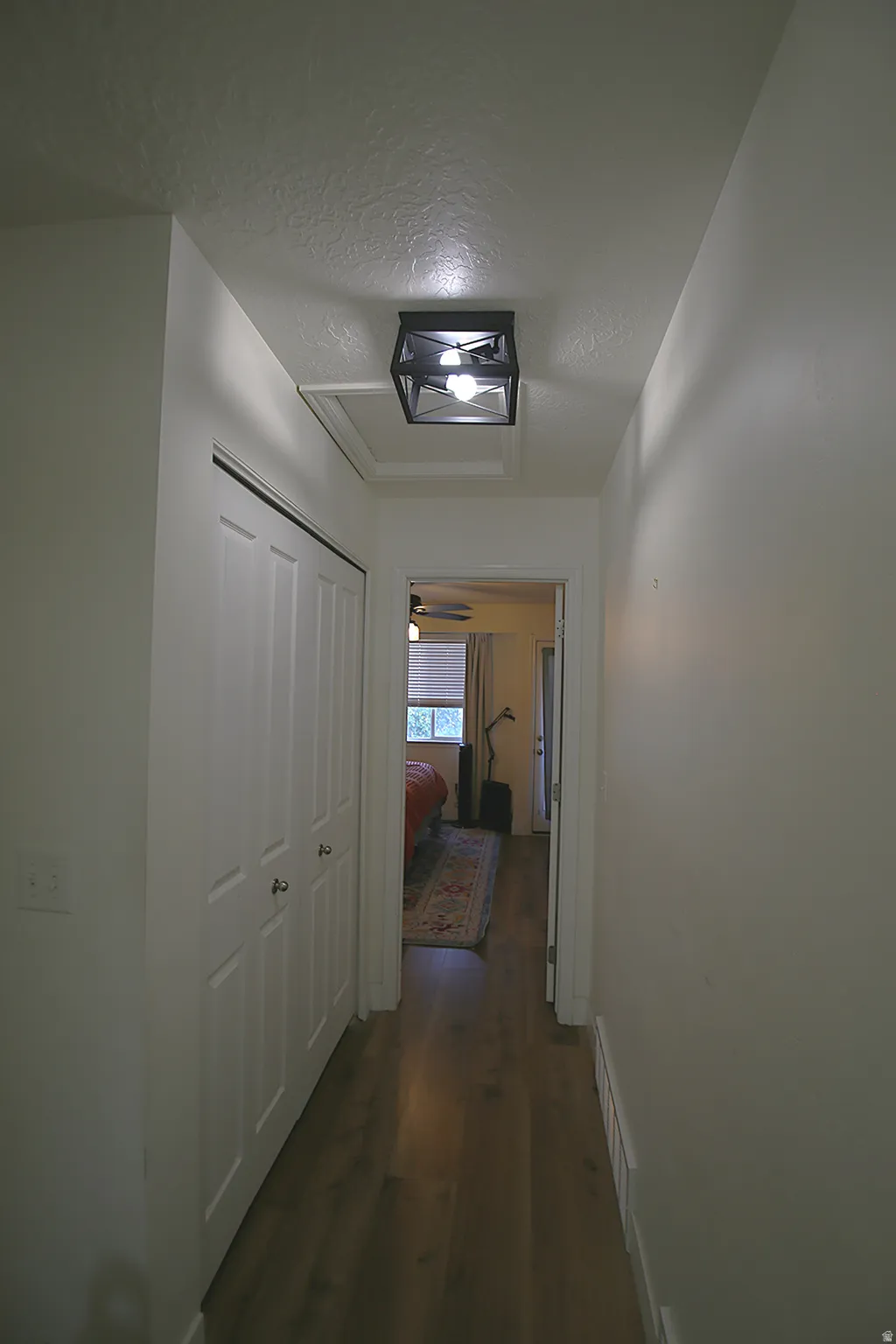 Hallway featuring wood-finish flooring, a modern flush-mount light fixture, and white bi-fold doors