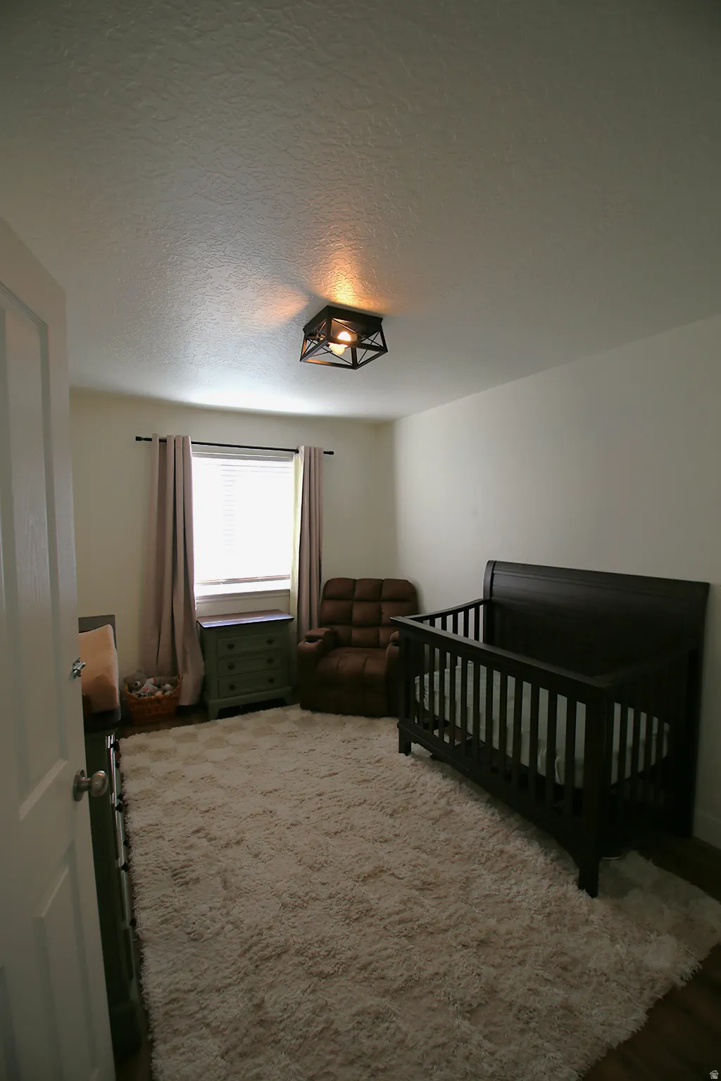 Room featuring a window with blinds and drapes, a ceiling-mounted light fixture, and wood-finish flooring