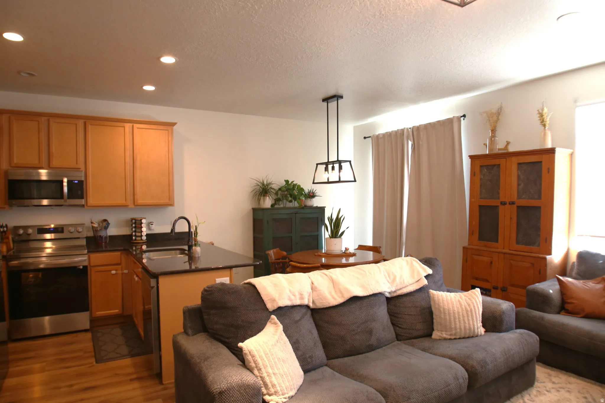 Open-concept living area featuring a kitchen with wood cabinetry, stainless steel appliances, and a dark countertop