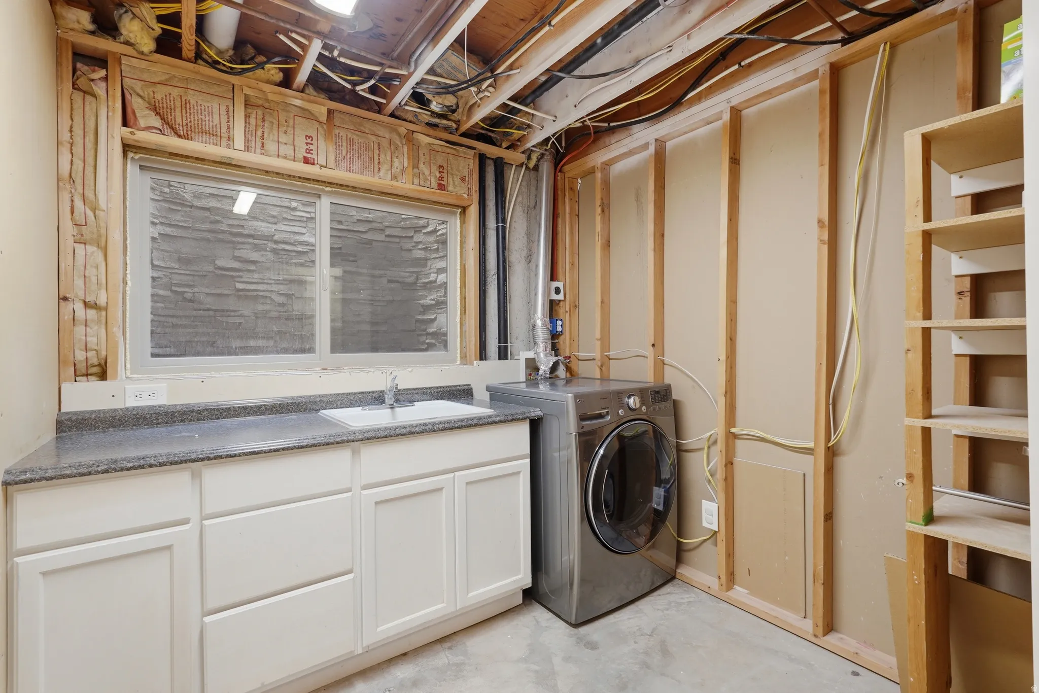 Utility space featuring a single-basin sink, laminate countertop, white cabinetry, and framed unfinished walls