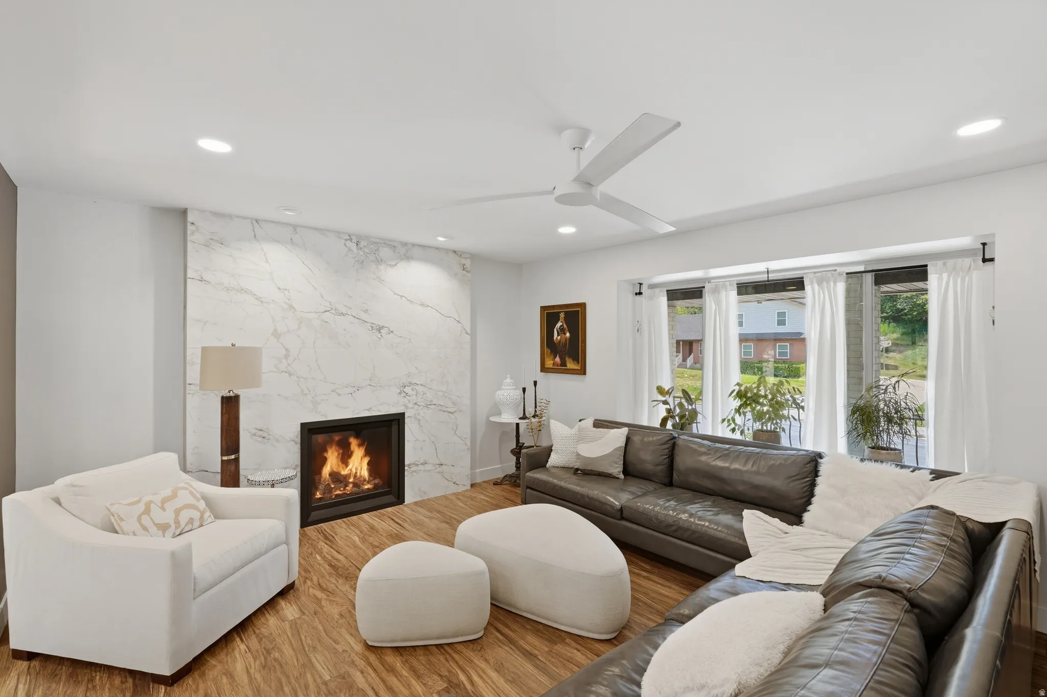 Living area featuring a modern linear fireplace with a full-height stone surround, wood-finish flooring, recessed lighting, a ceiling fan, and a wide window with multiple panes