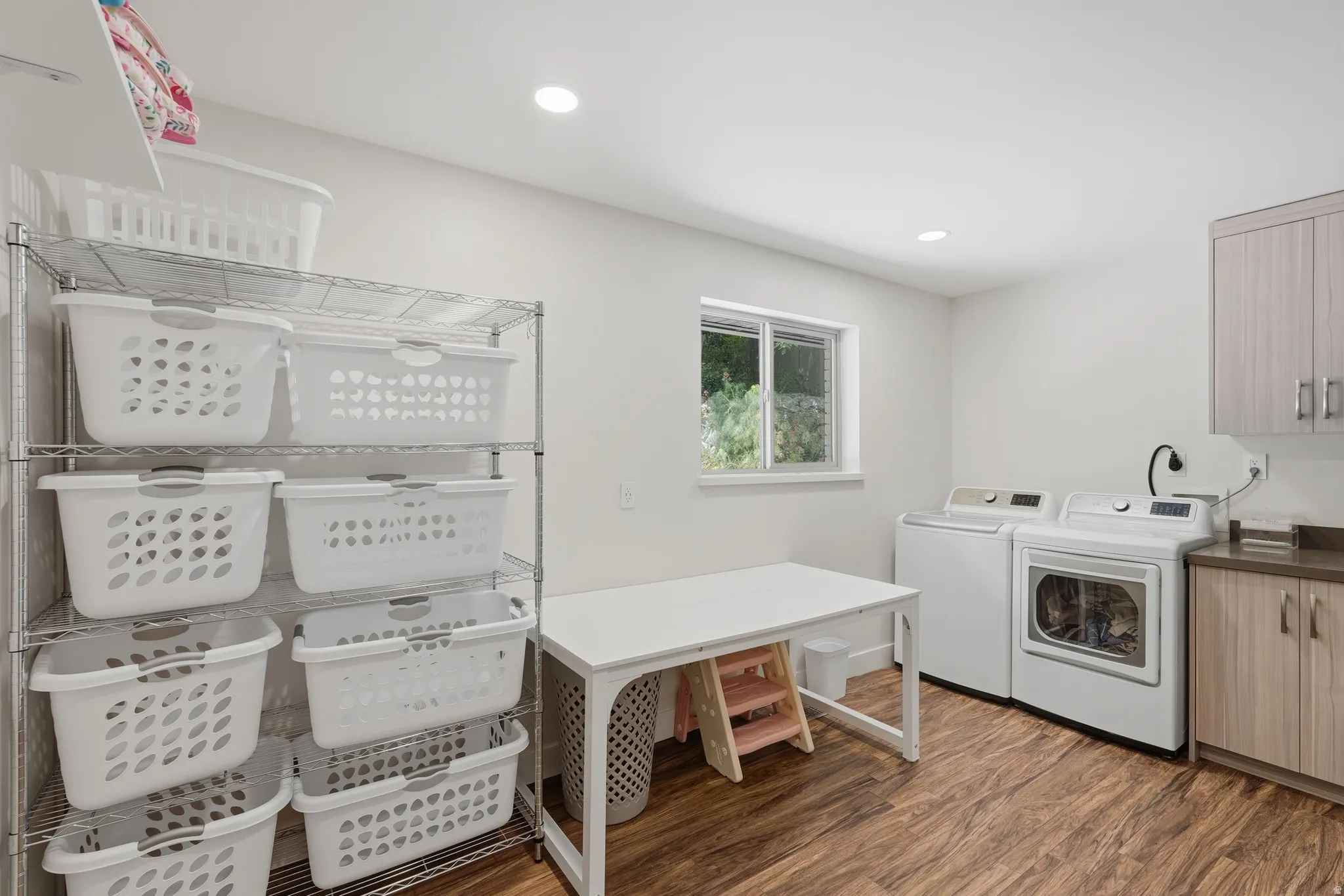 Dedicated laundry area featuring wood-finish flooring, a window providing natural light, recessed ceiling lighting, and built-in cabinetry with a countertop