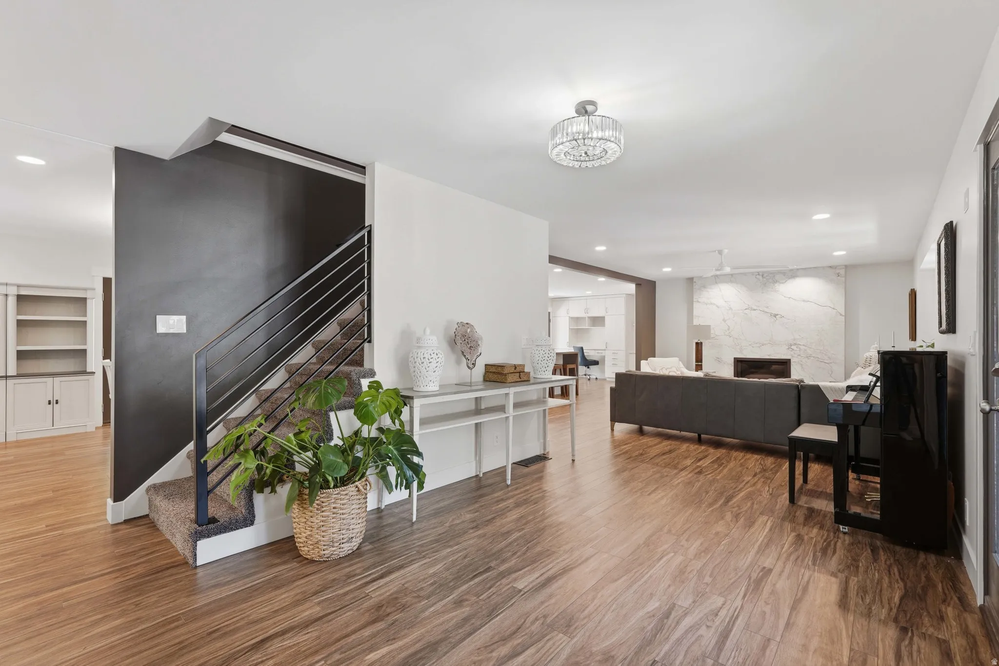 Open-concept living space with wood-finish flooring, a modern staircase with metal railings, and a fireplace featuring a large stone surround