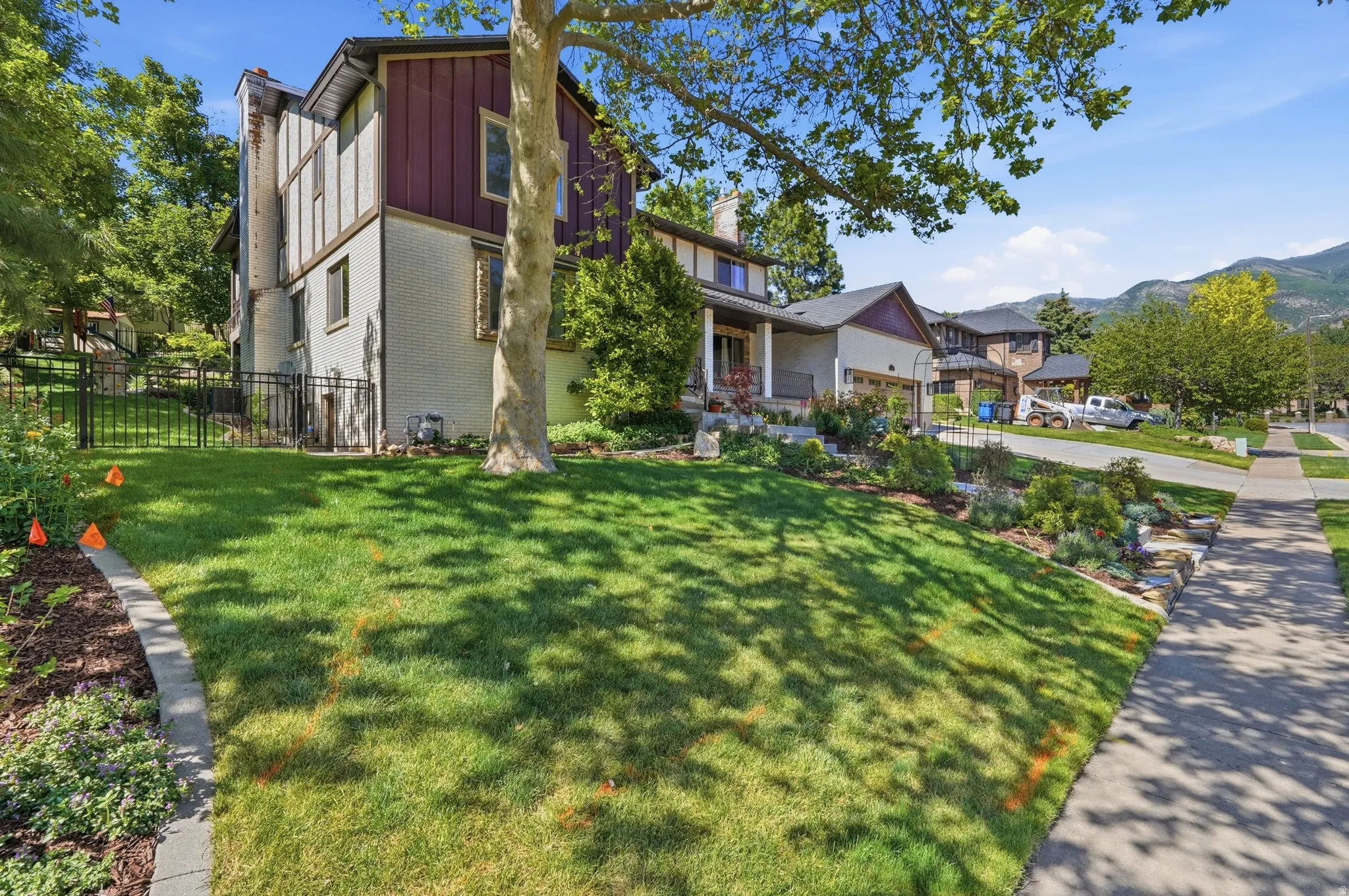 Terraced front yard with mature landscaping, a concrete sidewalk, and mountain backdrop