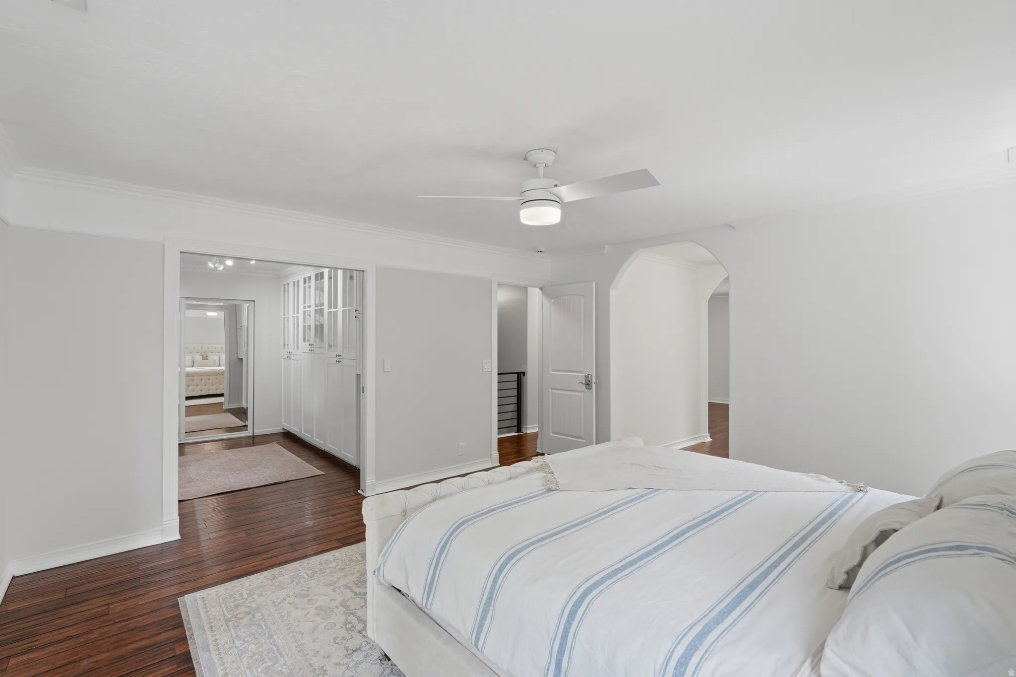 Spacious room featuring rich wood-finish flooring, a modern ceiling fan with integrated lighting, and crown molding