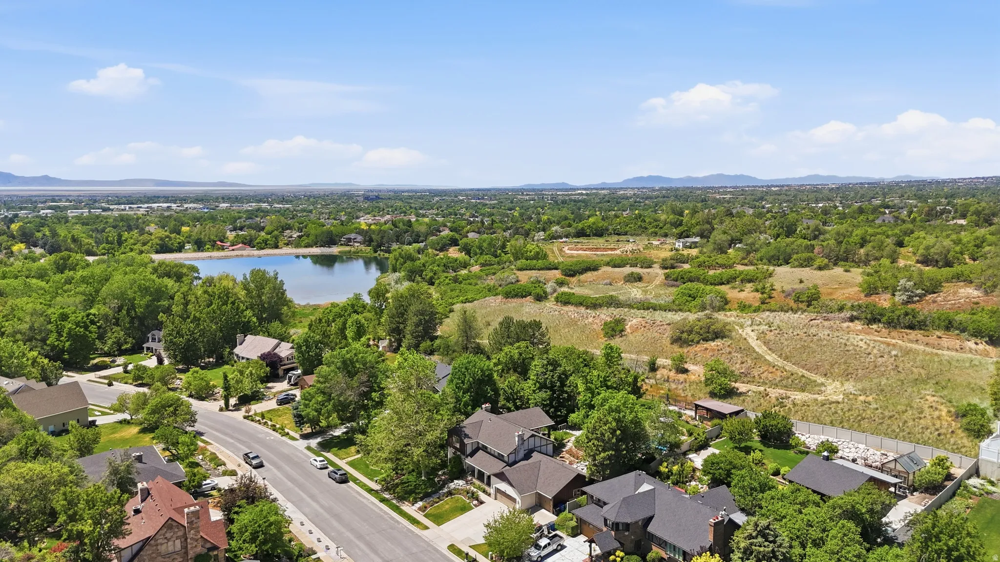 Aerial perspective showcasing a residential area with a prominent body of water, extensive tree canopy, and distant mountains