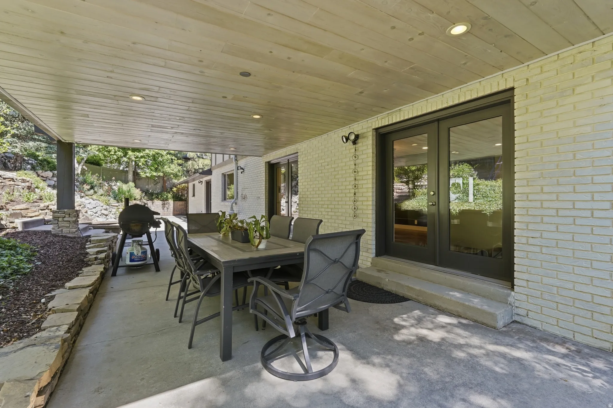 Covered patio featuring a wood-finish ceiling with recessed lighting, concrete flooring, and a stone retaining wall