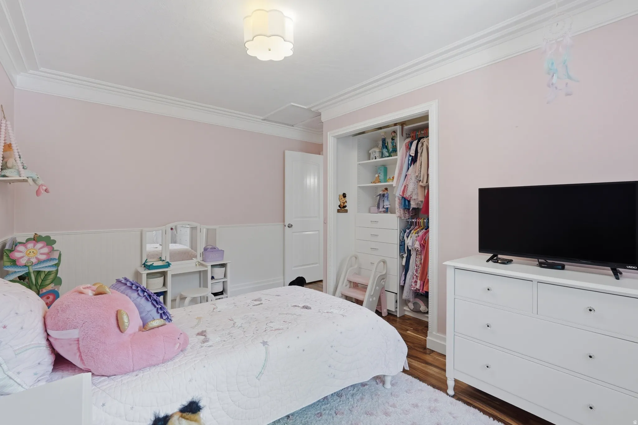 Bedroom featuring wood-finish flooring, crown molding, wainscoting, and a built-in closet organization system