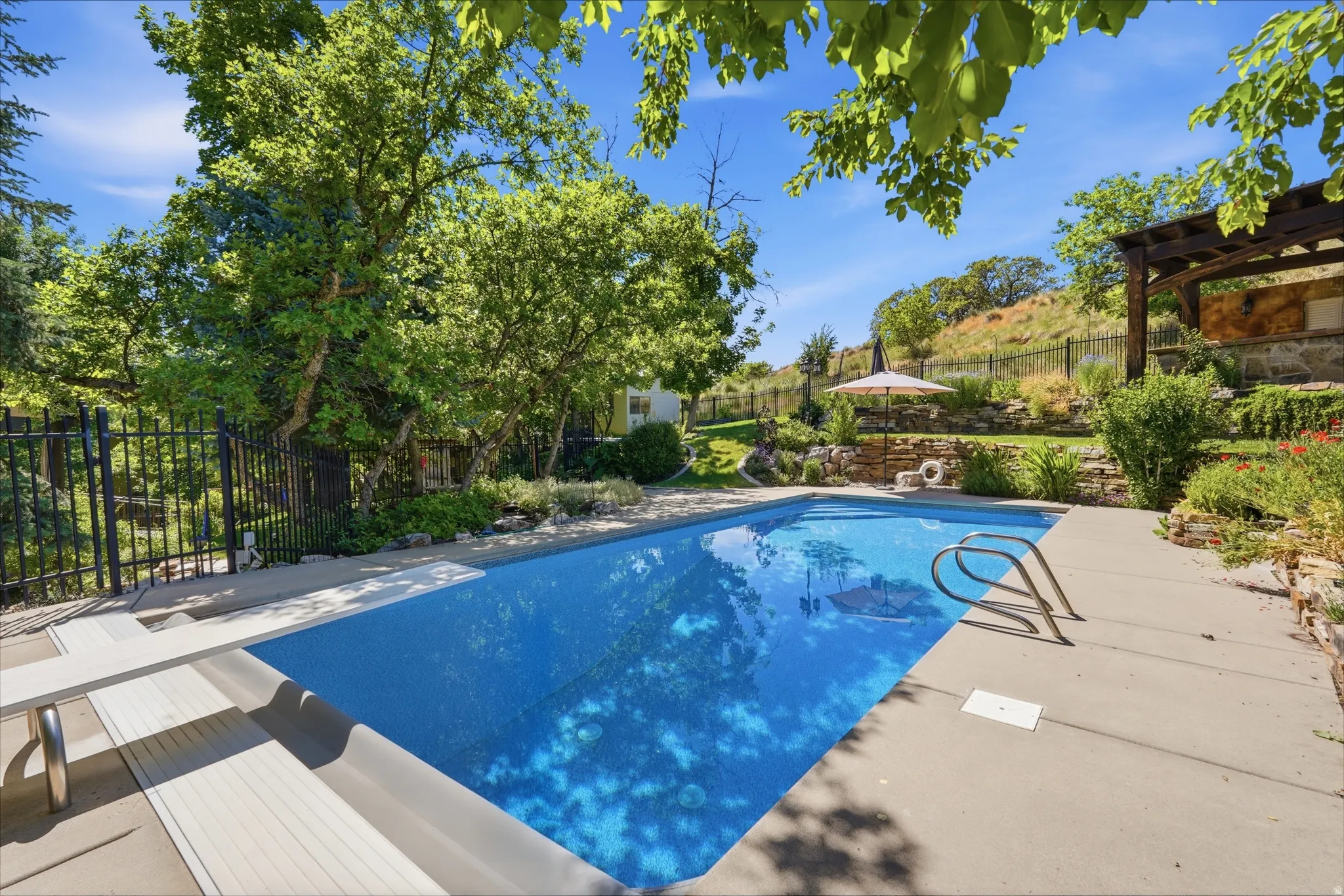 Outdoor swimming pool with concrete decking, a diving board, and integrated steps
