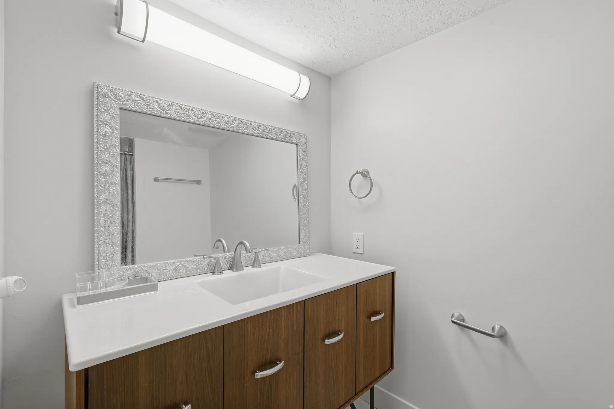Vanity area featuring a wood-finish cabinet with double sinks, light-toned countertop, and an ornate framed mirror