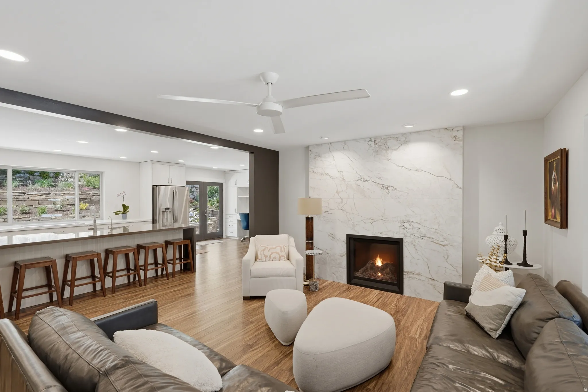 Open-concept living space featuring wood-finish flooring, a contemporary fireplace with a stone surround, and recessed lighting