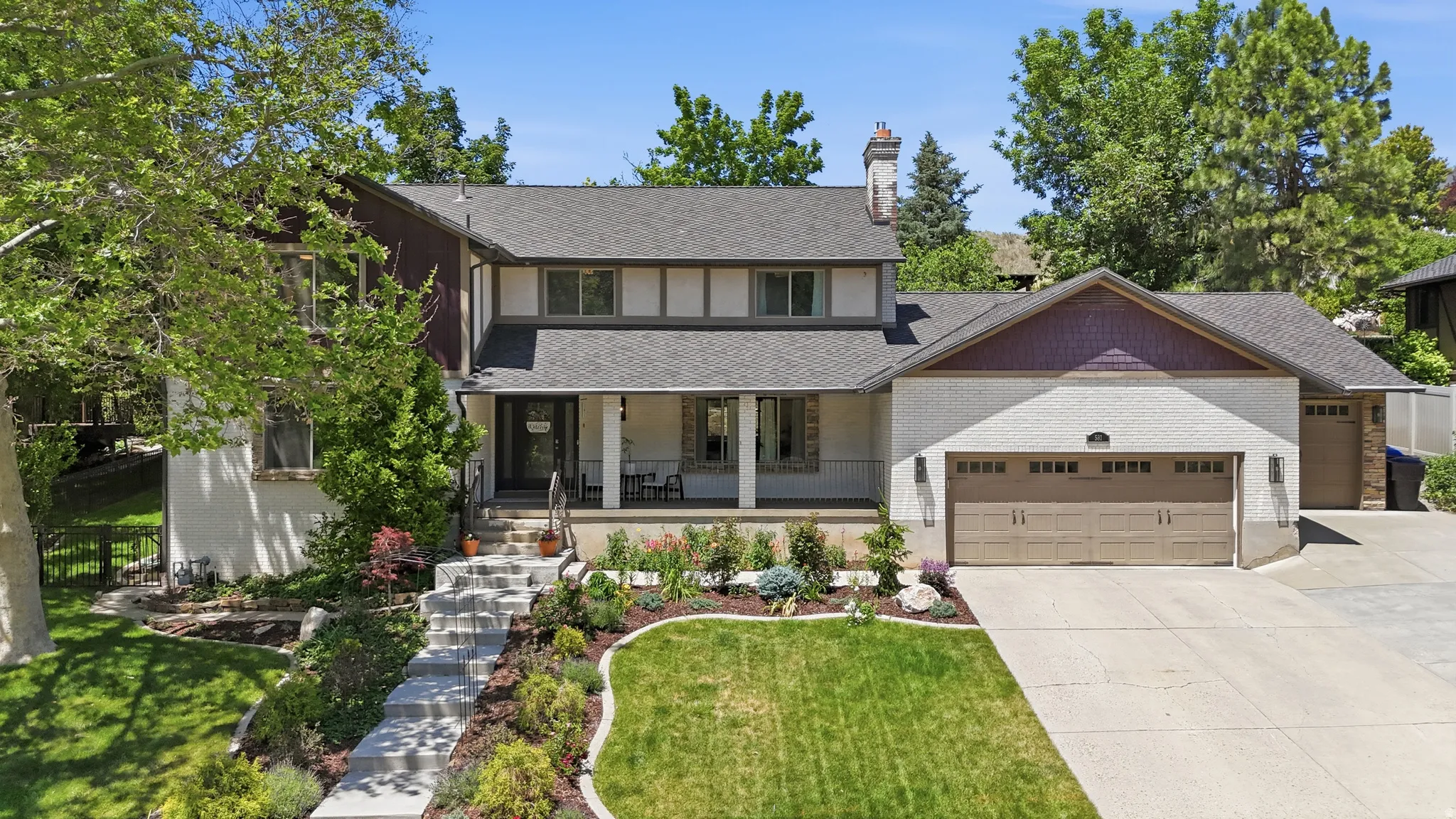 Traditional-style residence featuring a two-car garage with carriage-style doors, a covered front porch with white columns, and a terraced front yard with mature landscaping