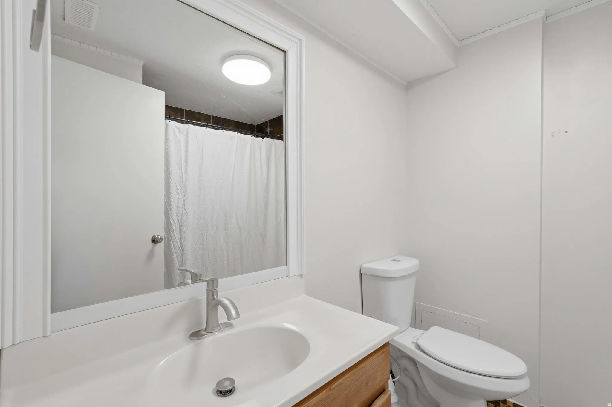 Bathroom featuring a white vanity with an undermount sink and brushed nickel faucet, a frameless wall mirror, and a white toilet