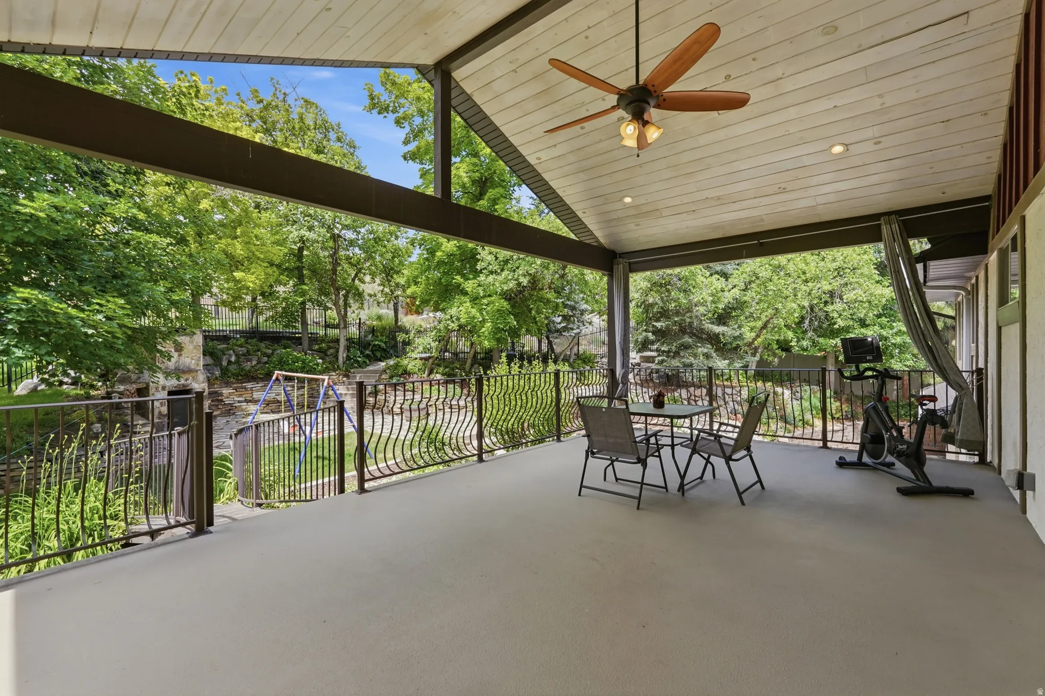 Spacious covered patio featuring a vaulted wood-finish ceiling, ceiling fan, recessed lighting, and ornate metal railings