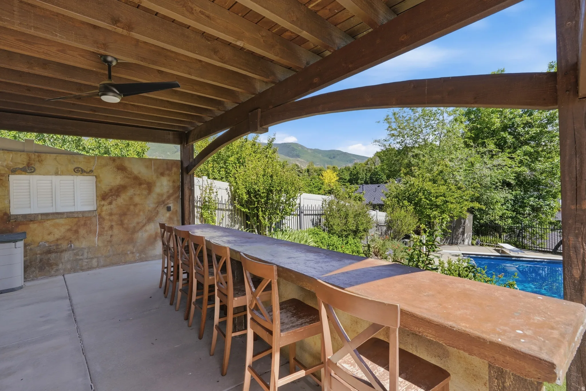 Covered outdoor entertaining area featuring a built-in bar, wood-beam ceiling, and ceiling fan