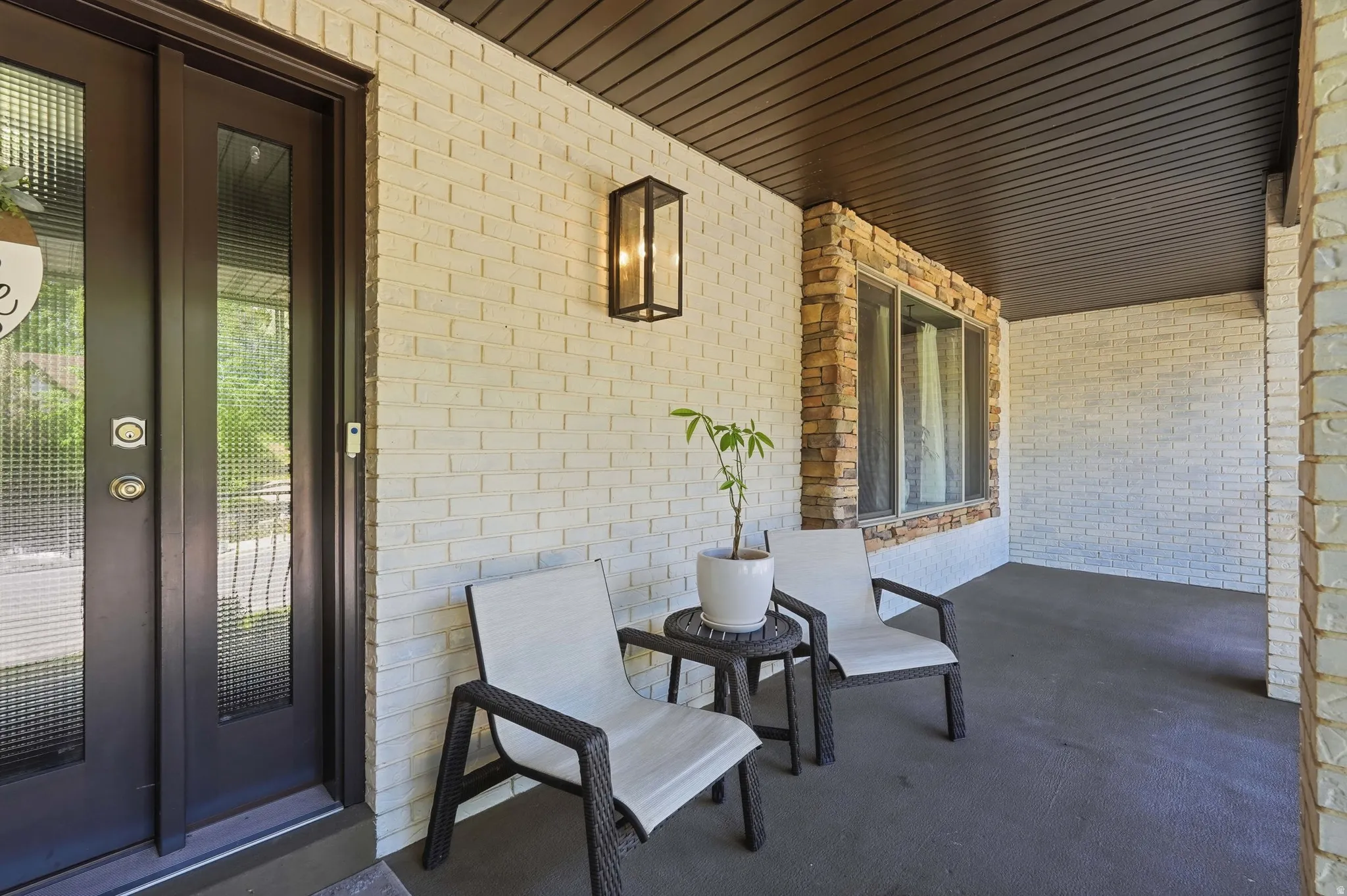 Covered porch entry featuring a double door with textured glass panels, light-colored brick facade, stone-accented window, and a dark-finished ceiling