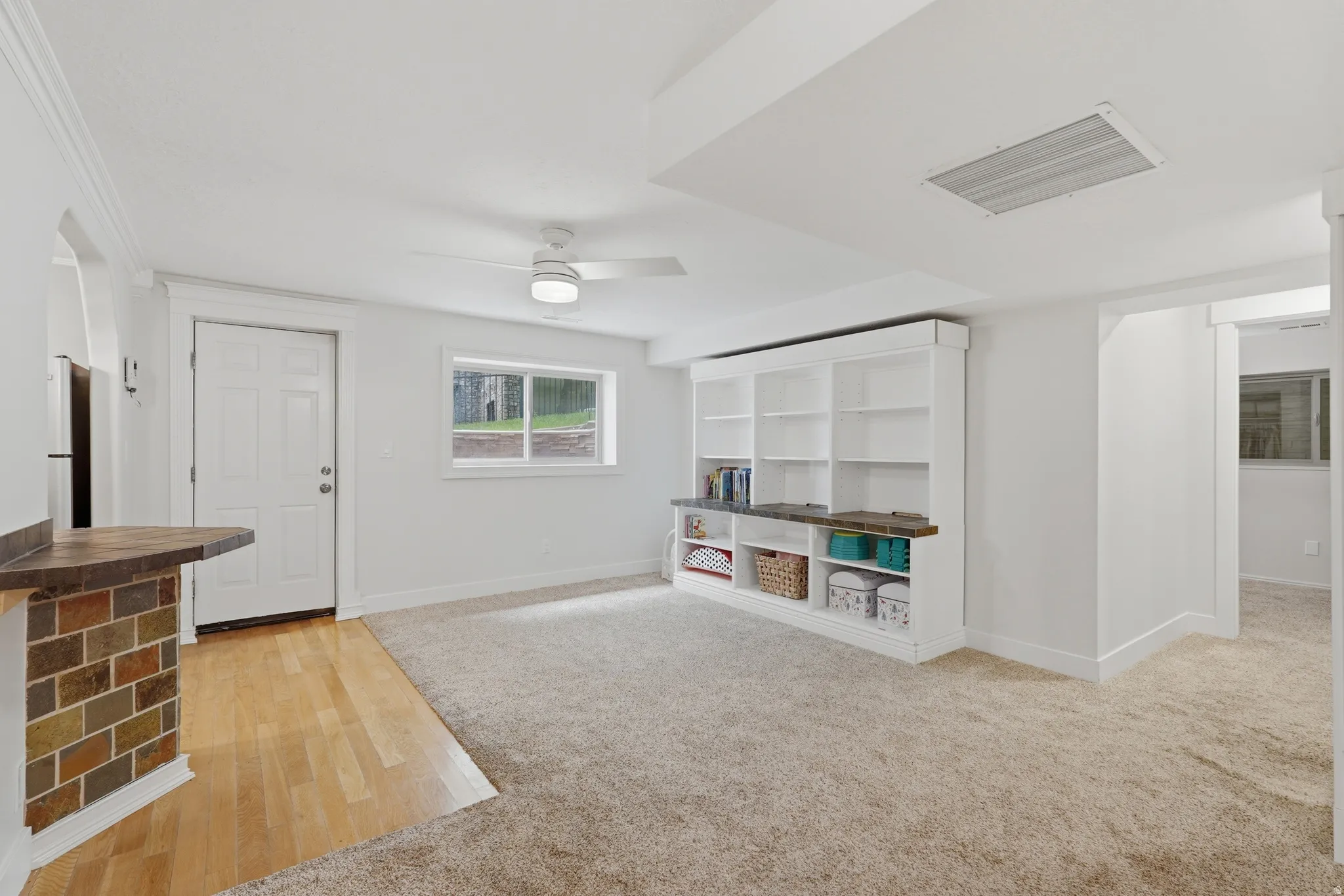 Spacious room featuring plush carpeting, a large built-in shelving unit with a desk area, and a ceiling fan