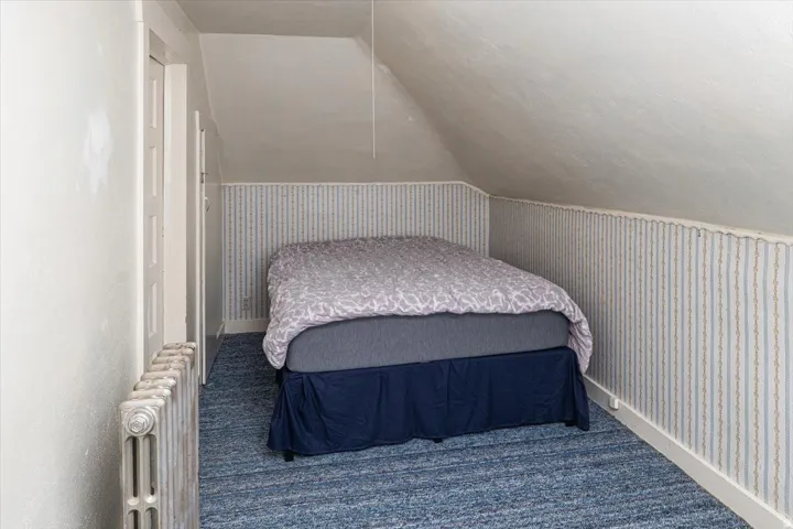 Attic room with sloped ceilings, striped wallpaper accent, blue carpet, and a cast-iron radiator