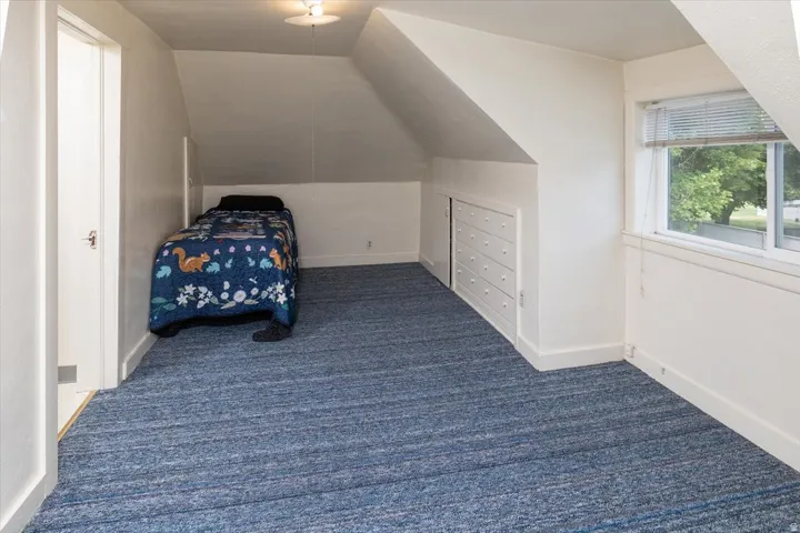 Room featuring sloped ceilings, blue patterned carpeting, a single window, and built-in white cabinetry