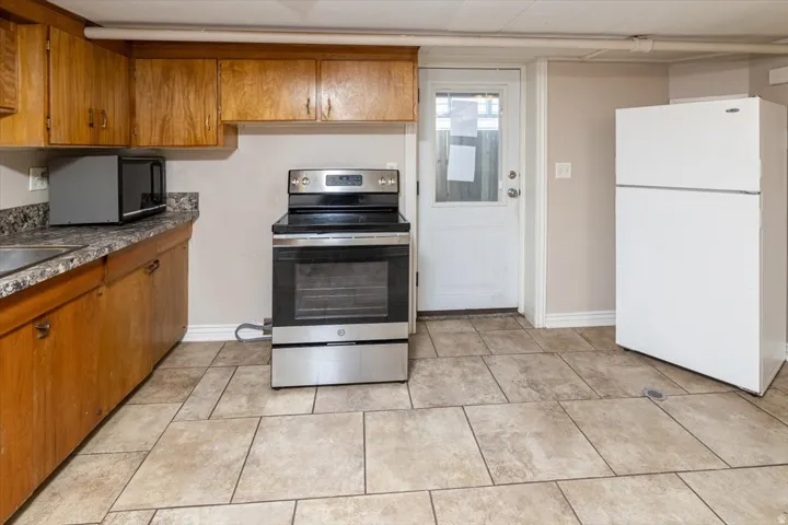 Kitchen featuring wood cabinetry, a stainless steel electric range, an integrated sink, a white exterior door, and large format floor tiling