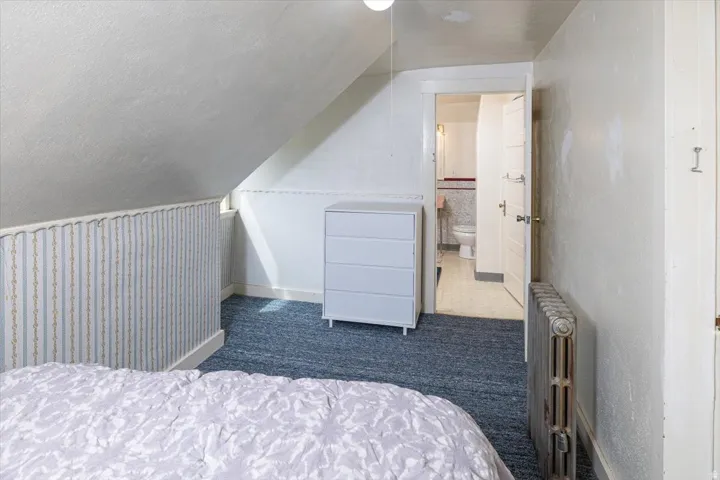 Sloped ceiling room featuring blue patterned carpeting and a partial view of a white tiled bathroom