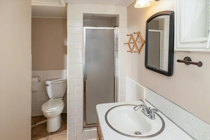 Bathroom featuring a vanity with an integrated sink, a rectangular mirror, a glass-enclosed shower, a toilet, and wall-mounted tile work