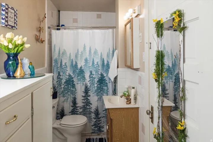 Bathroom featuring white subway tile surround, tile flooring, wood-finish vanity with an integrated sink, and a wall-mounted medicine cabinet